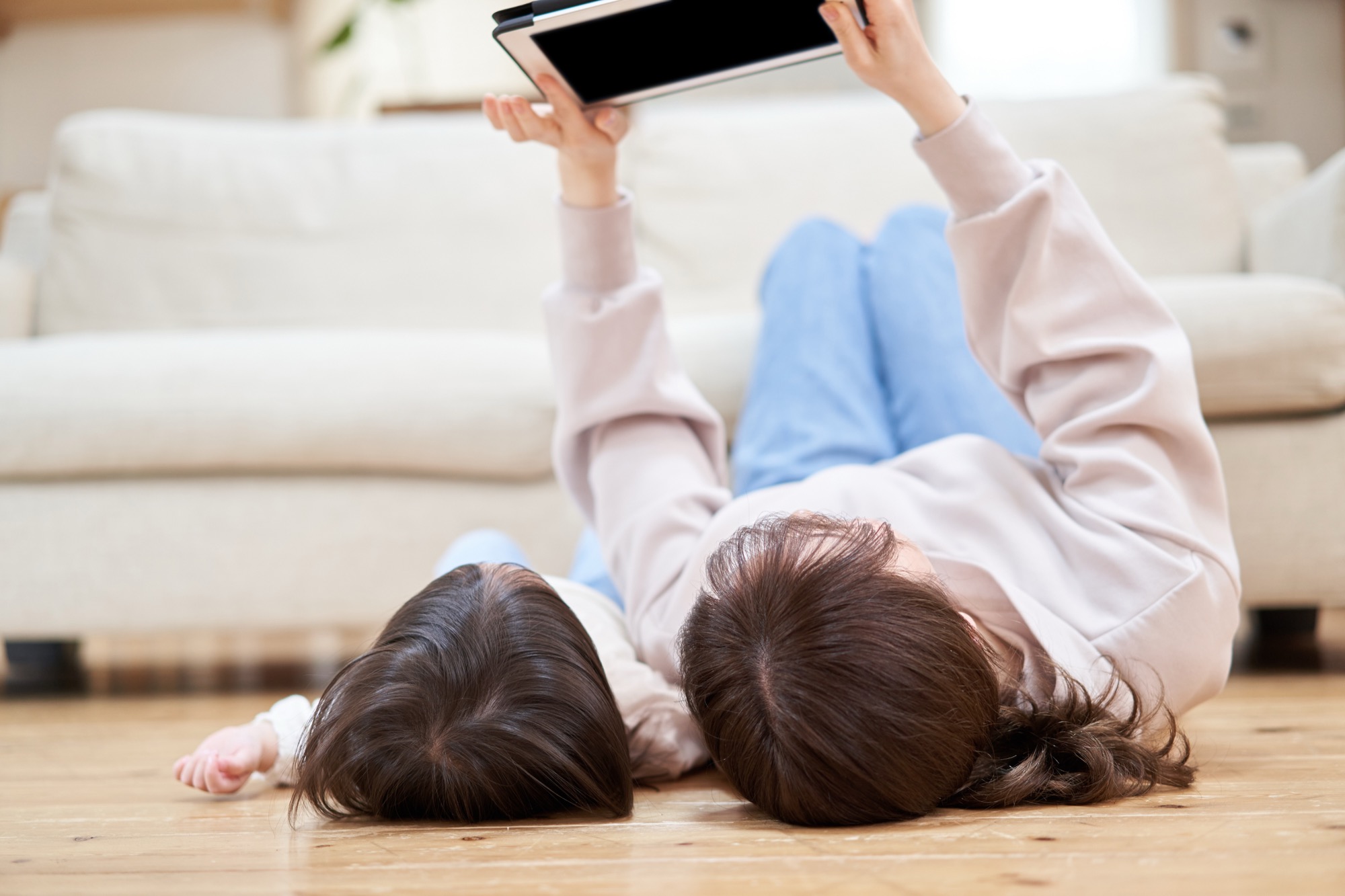 床暖房のフローリングに寝っ転がってタブレットを見る親子